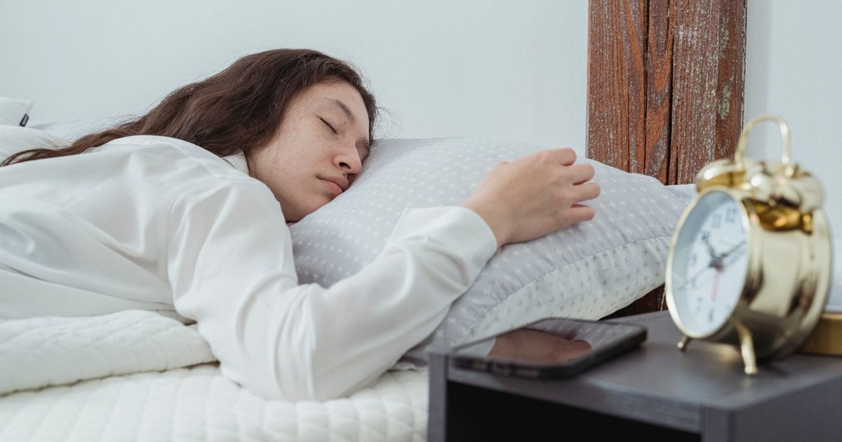 A woman asleep on a white pillow beside a bedside alarm clock.