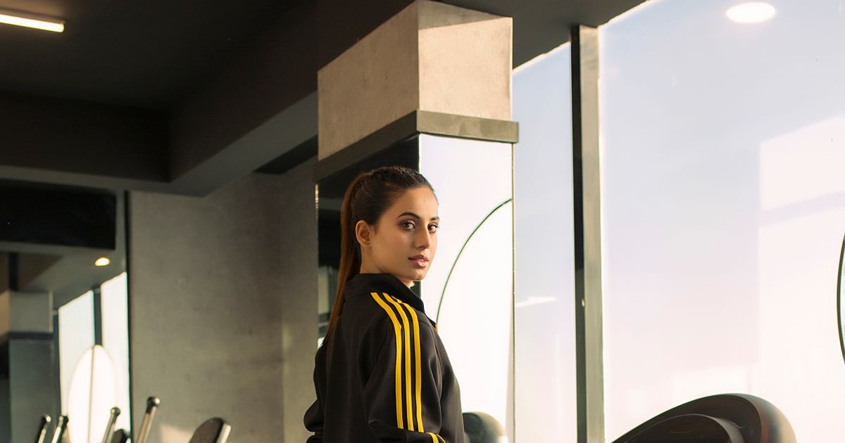 A woman stepping onto a treadmill in a gym.