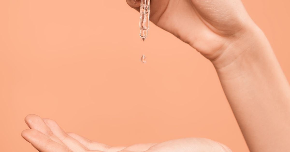 A serum dropper releasing a drop of skincare product above an open hand.
