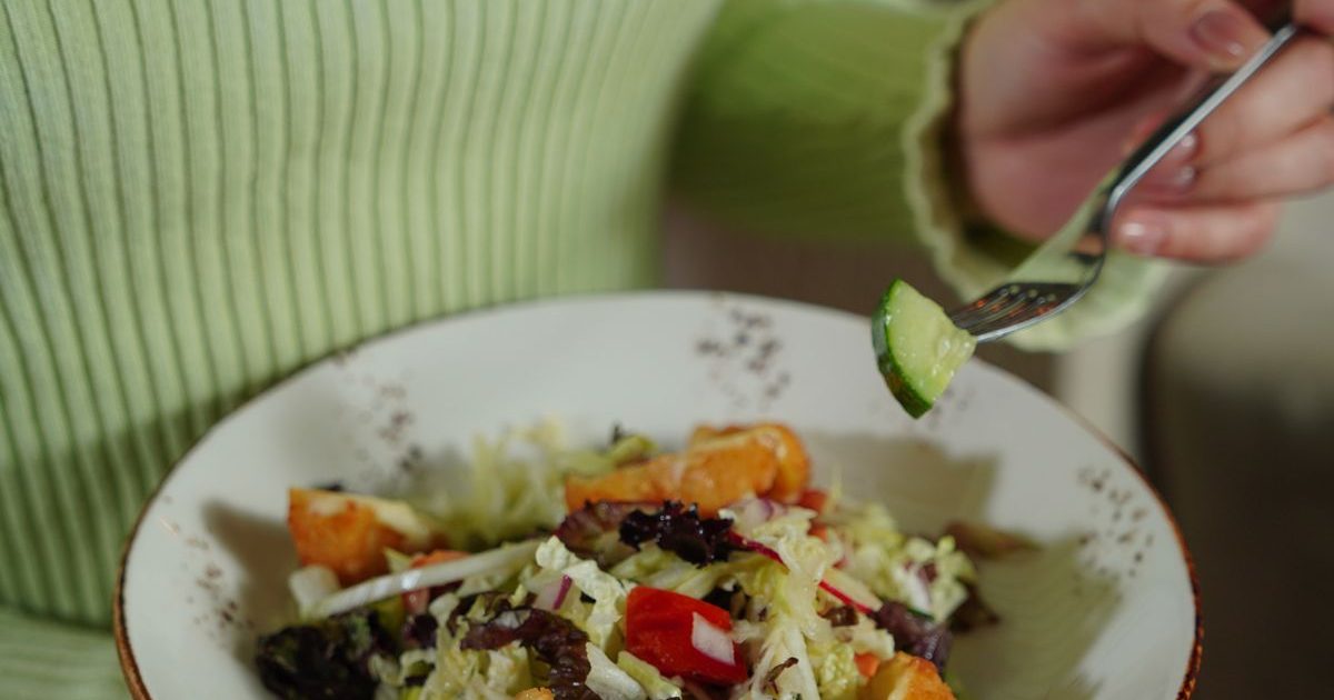 A woman eating a colourful salad from a bowl.