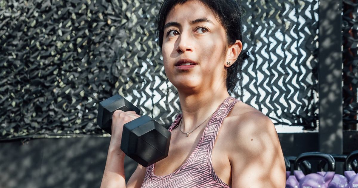 A woman lifting a dumbbell during a strength workout in a gym.